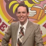 A still from Guy Montgomery's Guy Mont-Spelling Bee showing Guy Montgomery smiling at his podium