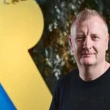 Craig Duncan poses in front of a Rare logo.