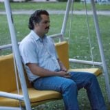 A guy from Narcos sits on a bench.